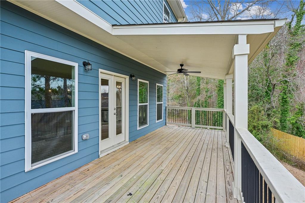 Covered wooden deck along a blue-sided house, with white railings and trees beyond.