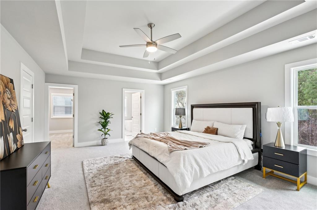 Staged bedroom with a king-size bed beneath a tray ceiling and large windows.