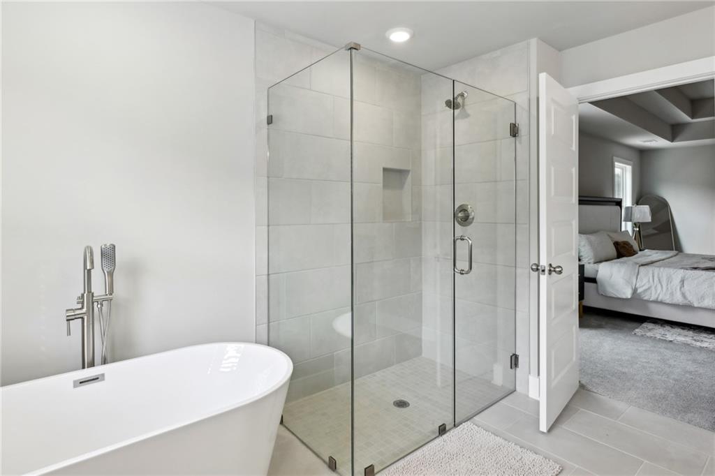 Bathroom with a freestanding tub and glass-enclosed tiled shower beside an open bedroom doorway.