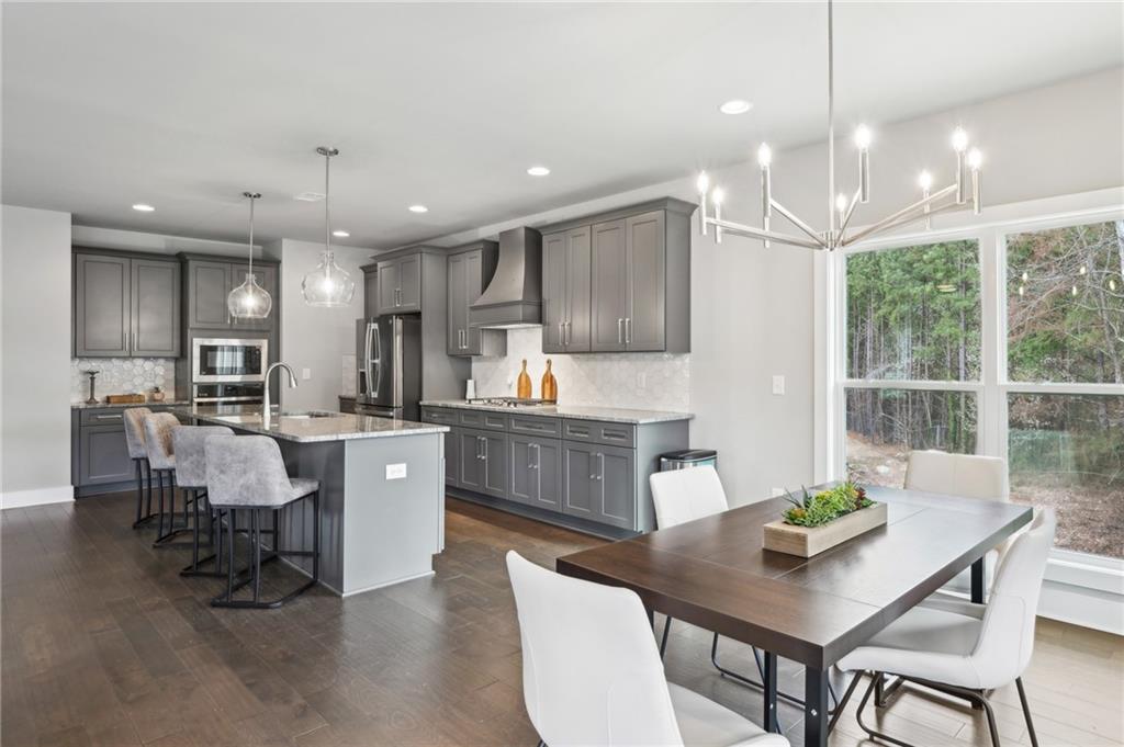 Open-plan kitchen with gray cabinets and island adjoining a dining area with large windows overlooking trees.