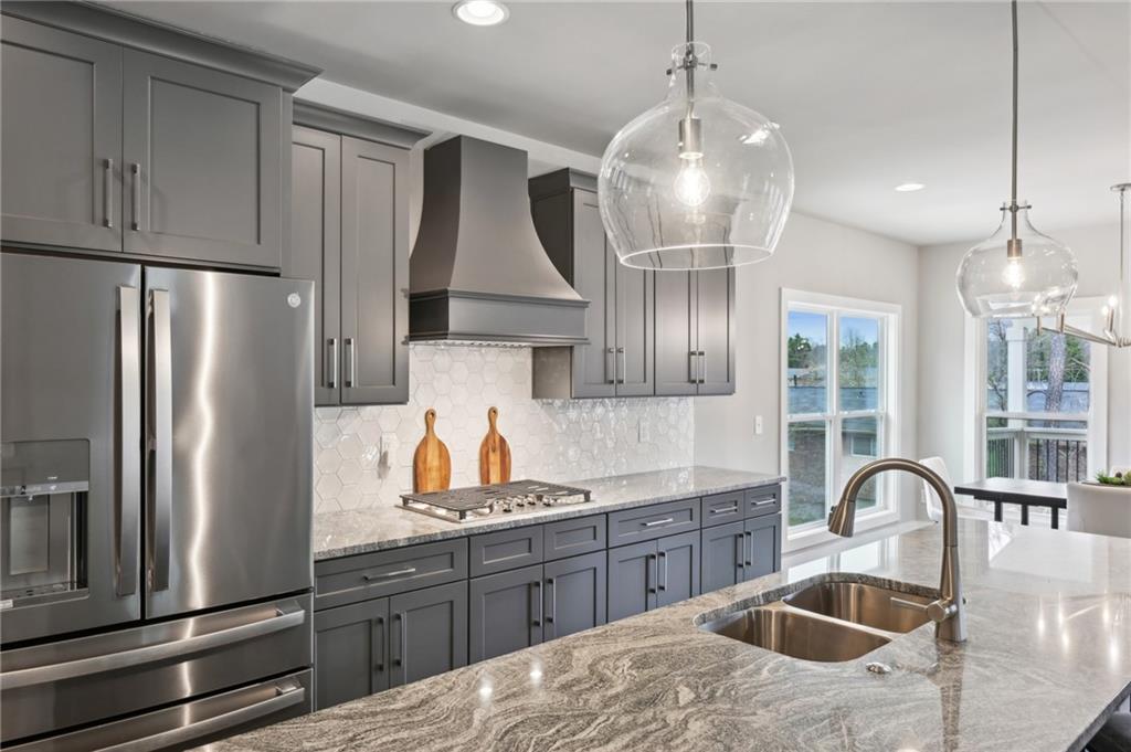 Kitchen with gray cabinets, stainless steel appliances, and a veined stone island overlooking water.