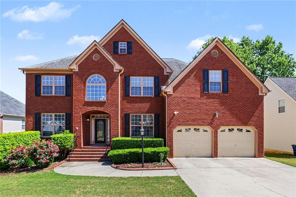 Two-story red brick house with a gabled façade, arched window, and two-car garage.