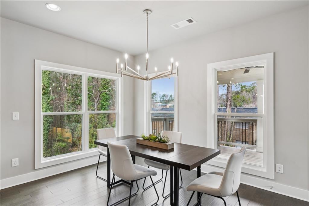 Dining room with a dark table, white chairs, modern chandelier, and large windows overlooking trees.