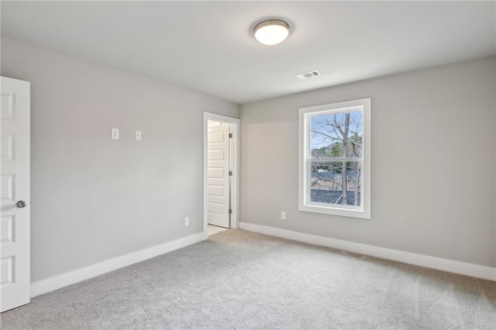 Empty bedroom with gray walls, pale carpet, and a window overlooking trees and rooftops.