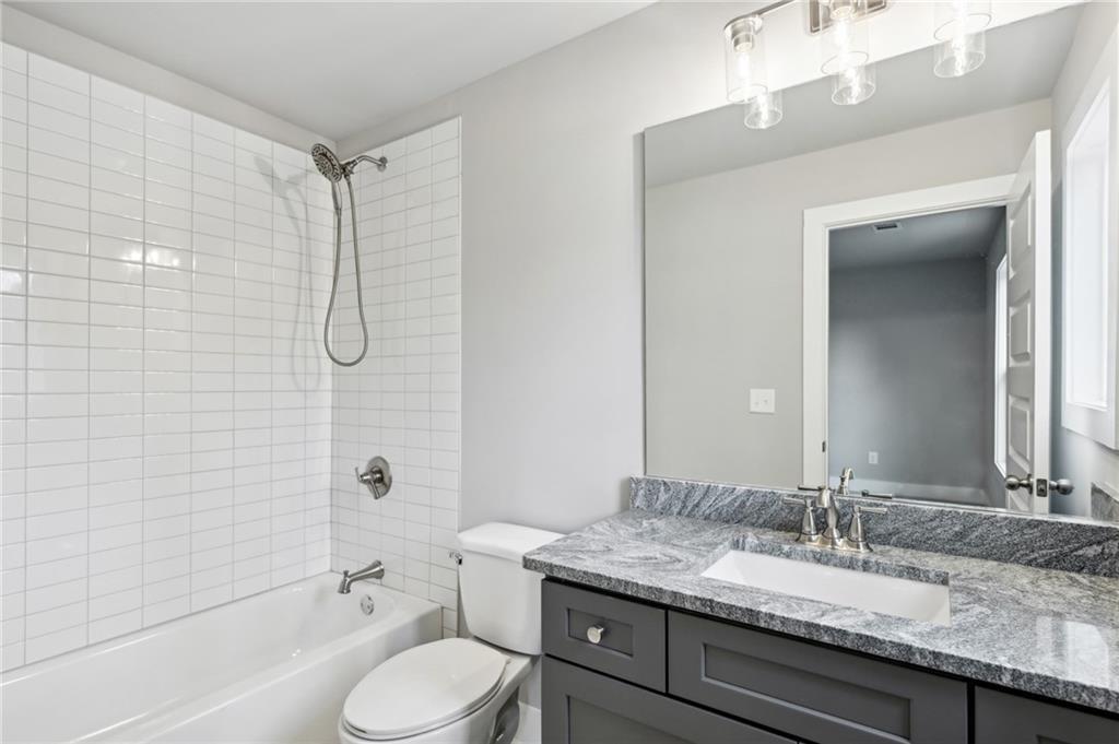 Bathroom with a white tiled tub and shower beside a dark gray stone-top vanity.