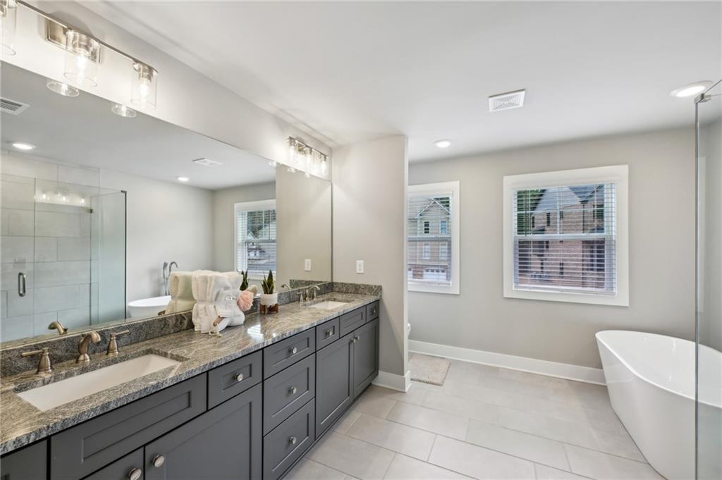 Bright bathroom with a dark double vanity, glass shower, and freestanding tub by the windows.