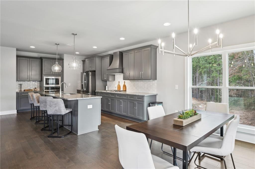 Open kitchen with gray cabinets and island adjoining a dining area beside large windows overlooking trees.