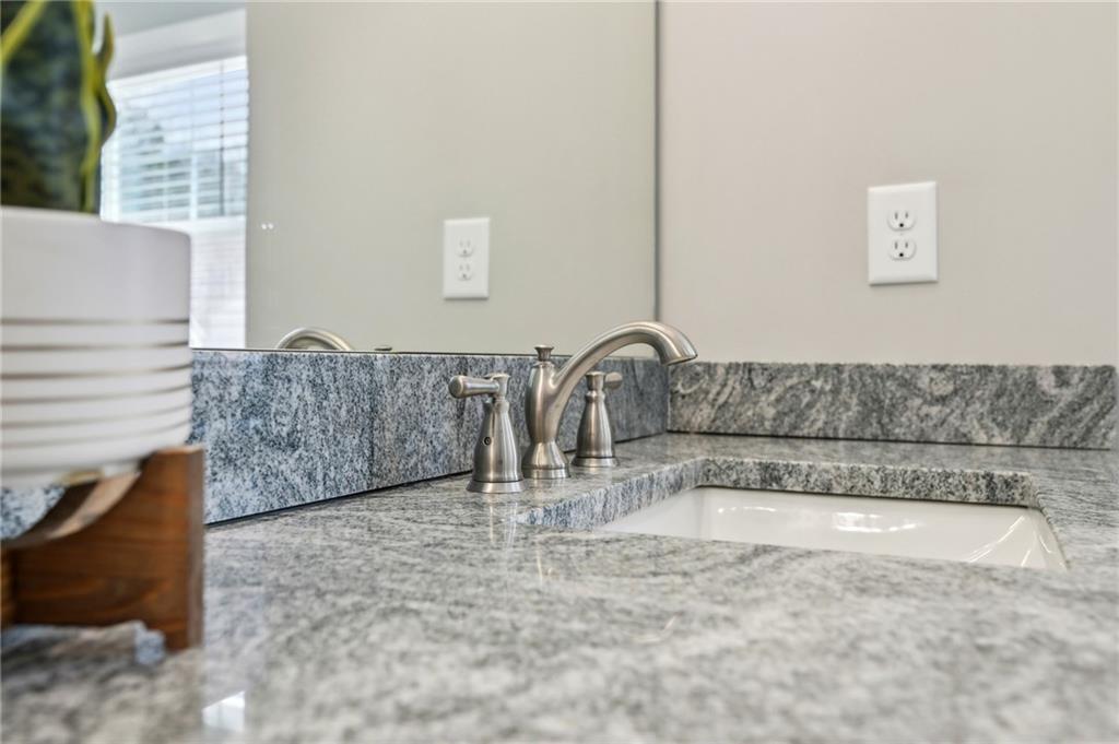 Bathroom vanity with a white sink, brushed-metal faucet, and gray granite countertop.
