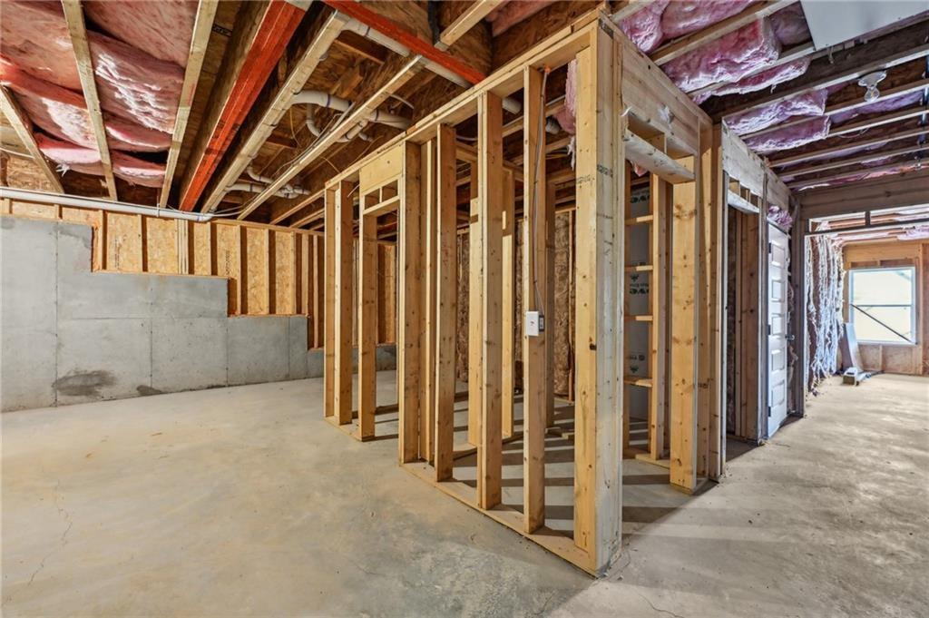Unfinished basement with exposed wood framing, concrete floor, and pink ceiling insulation.