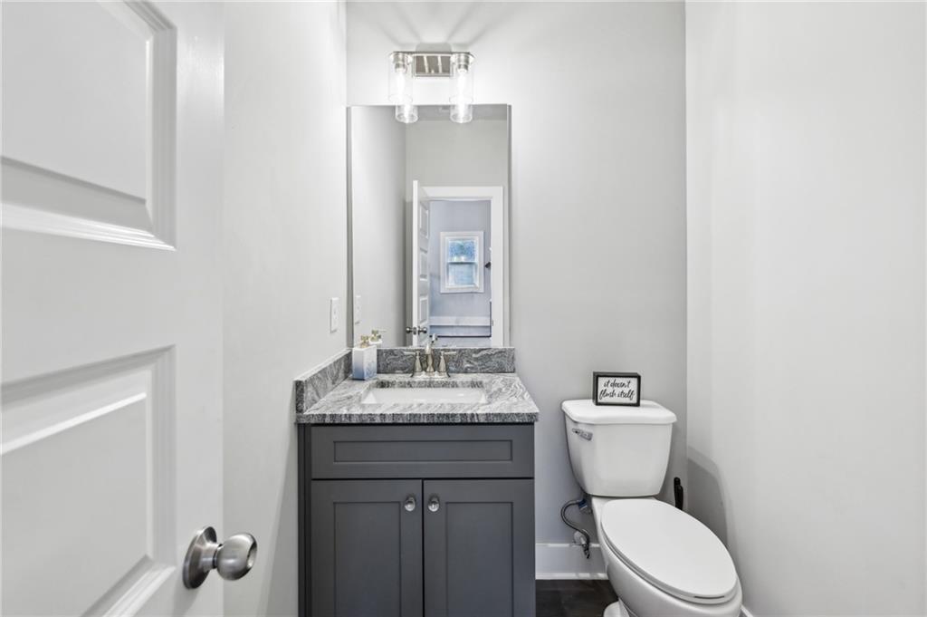 Bathroom with a dark gray vanity, stone countertop, large mirror, and white toilet.