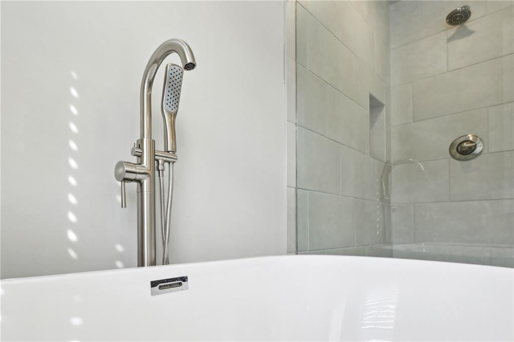White bathtub with a handheld showerhead beside a light tiled shower enclosure.