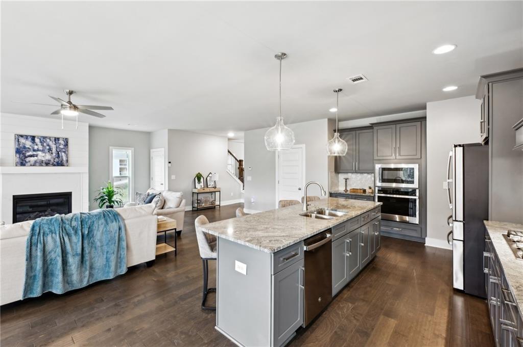 Open-plan kitchen and living room with a large stone island, gray cabinets, and fireplace.