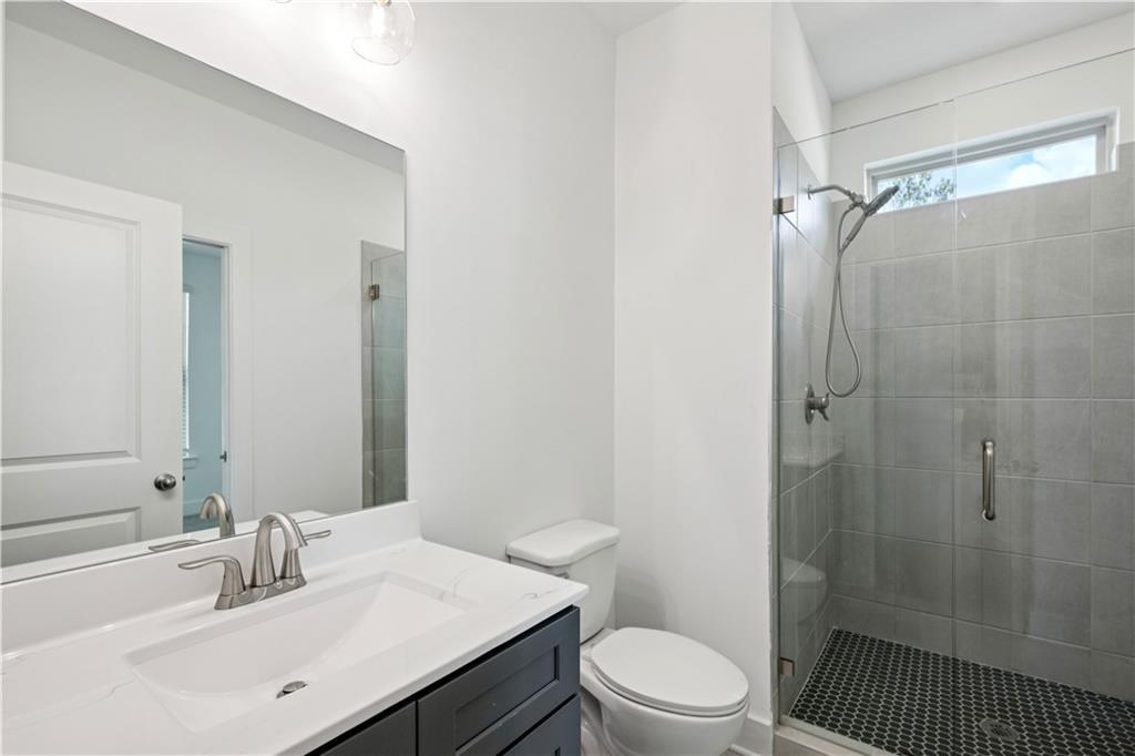 Bathroom with a dark vanity, white sink, and glass-enclosed gray-tiled shower.