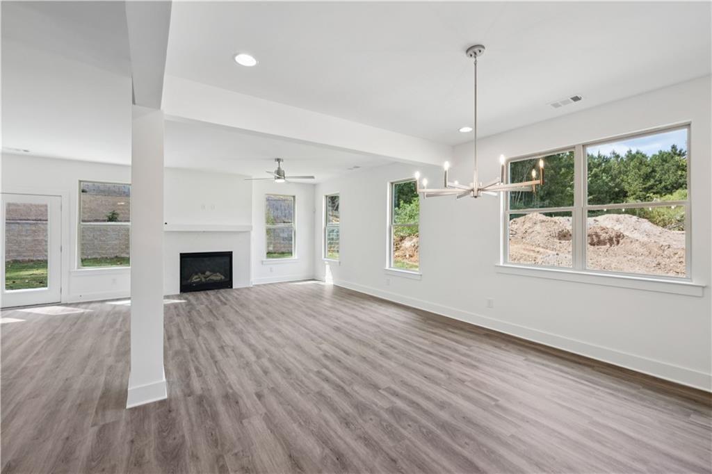 Vacant open-plan living area with gray plank floors, a fireplace, large windows, and a modern pendant light.