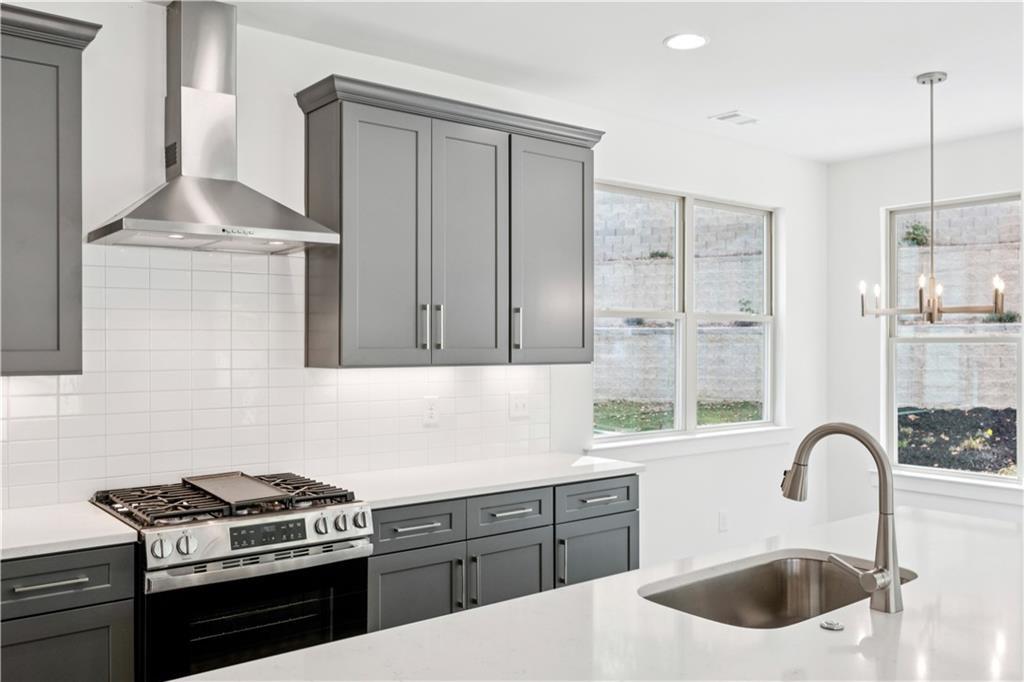Modern kitchen with gray cabinets, stainless-steel range, and a large island sink.