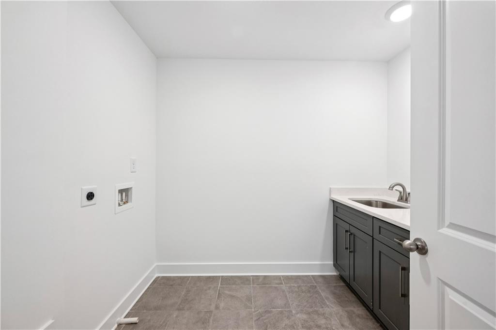 Empty laundry room with washer hookups, gray tile flooring, and a dark sink vanity.