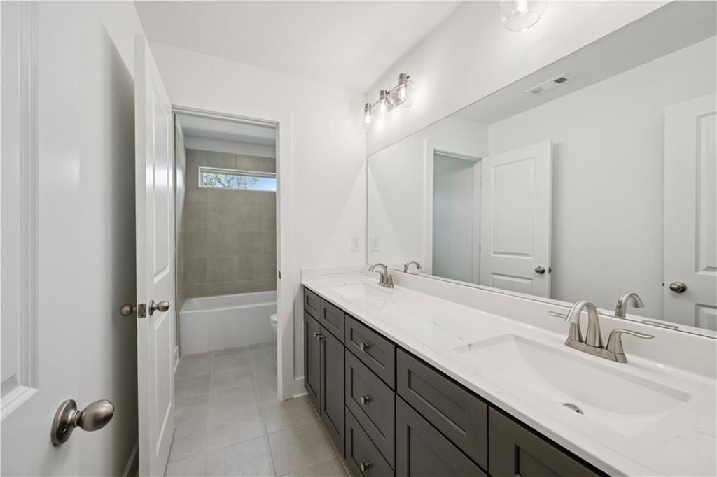 Bathroom with a long double vanity and tiled bathtub alcove with a narrow window.