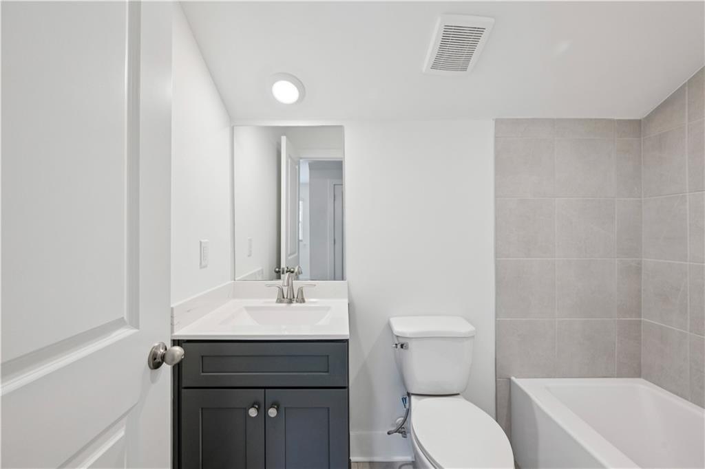 Bathroom with a dark gray vanity, toilet, and gray-tiled tub surround.
