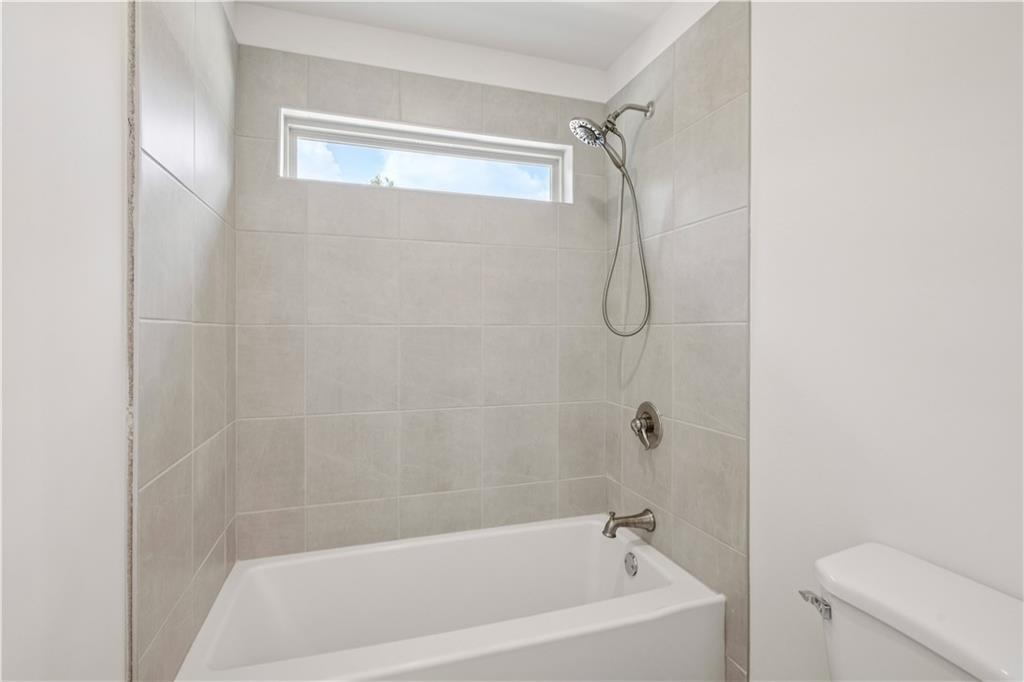 Bathroom with a white tub and shower, light-gray tile, and a narrow high window.