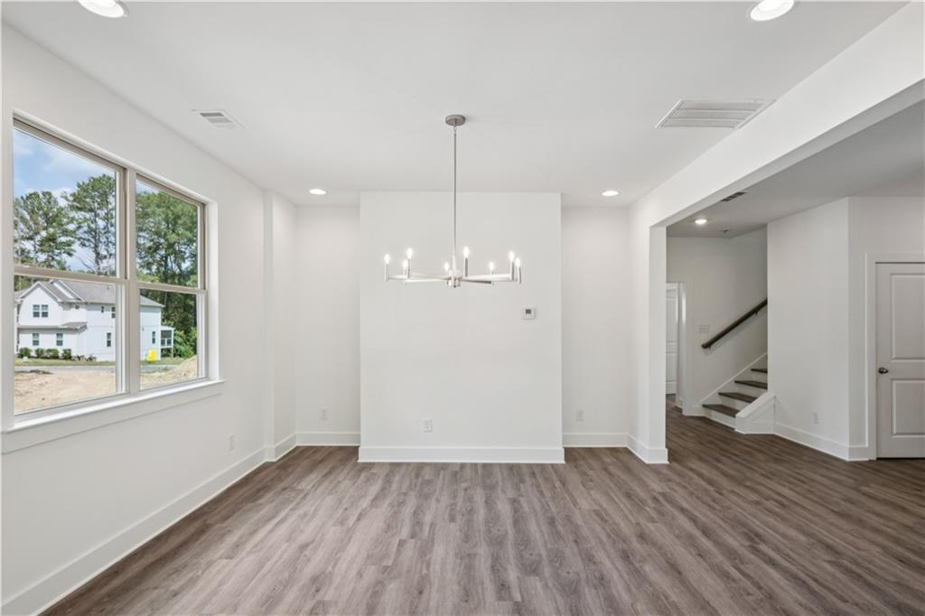 Vacant dining area with a modern chandelier, gray flooring, large windows, and an open staircase.
