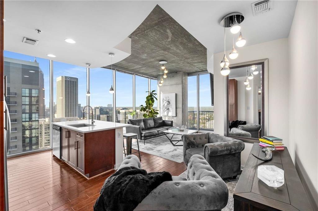 Furnished condo living room and kitchen with floor-to-ceiling windows overlooking the city skyline.