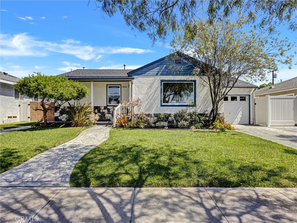 Single-story white house with blue trim, landscaped lawn, curved stone walkway, and attached garage.