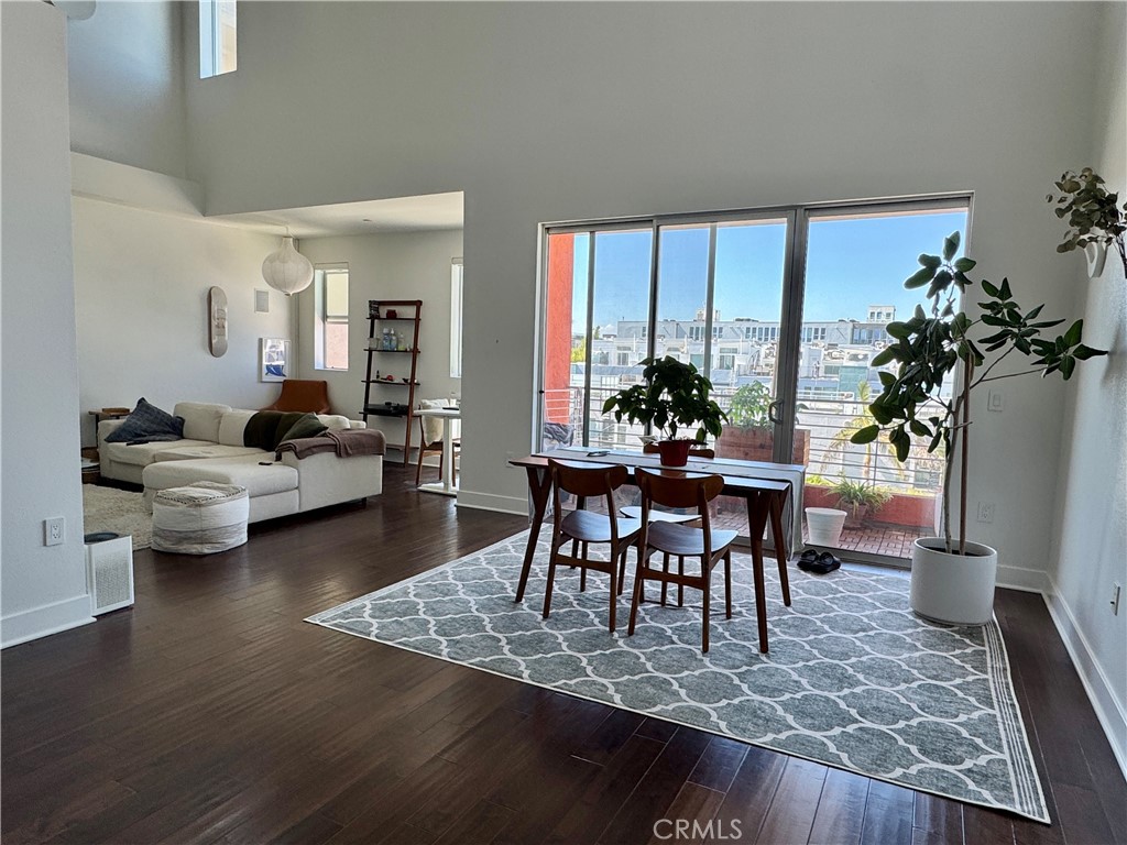 Open-plan living and dining room with a white sectional, patterned rug, and glass doors to a balcony.