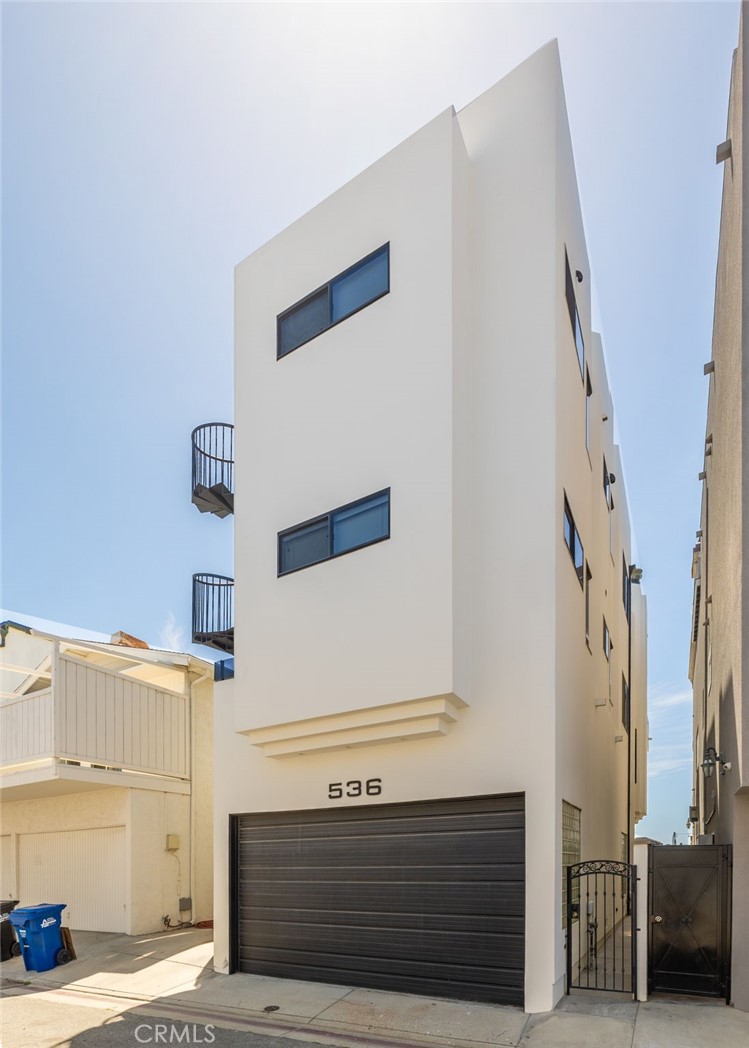 Modern white multi-story residence with a black garage door and small rounded balconies.