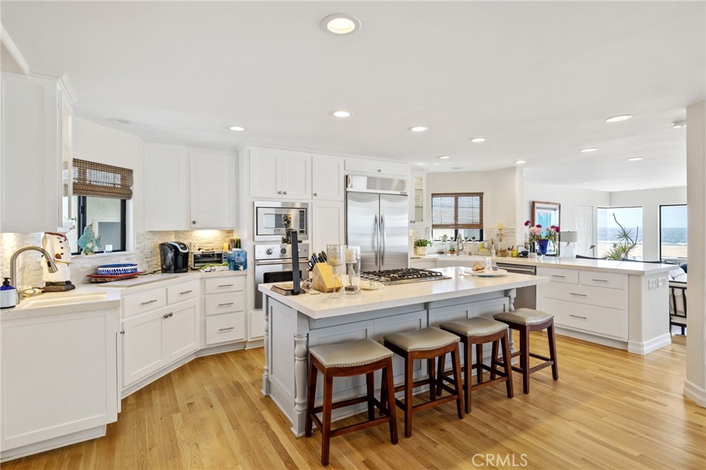 Open kitchen with white cabinetry, a large island with bar stools, and ocean views through the windows.