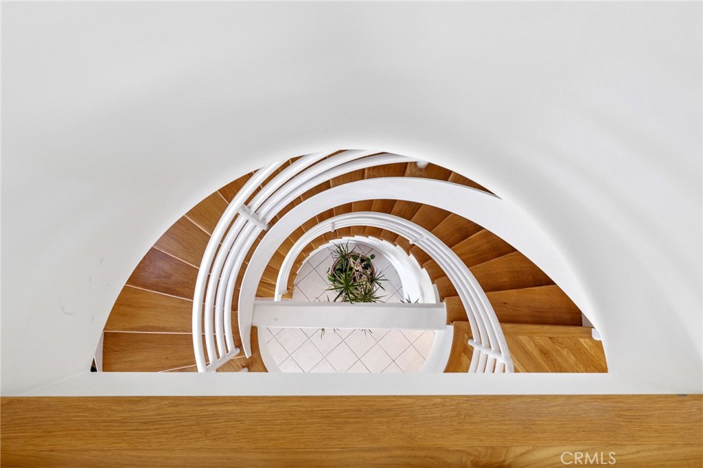 Curved wooden staircase with white railings overlooking a tiled landing and indoor plant.