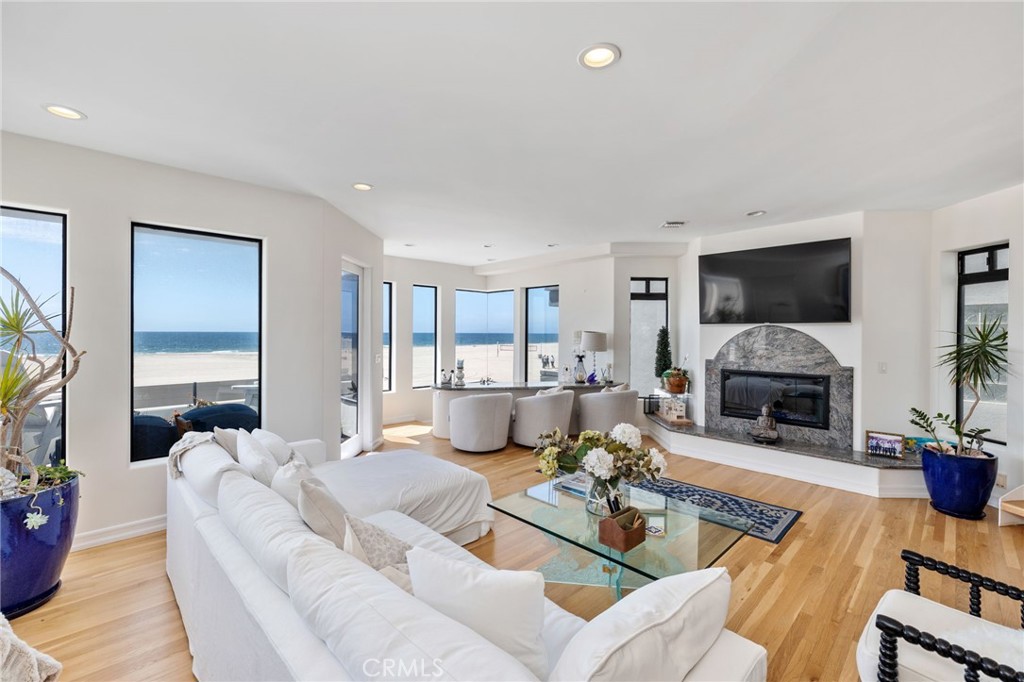 Oceanfront living room with white sofas, a stone fireplace, and broad beach and ocean views.