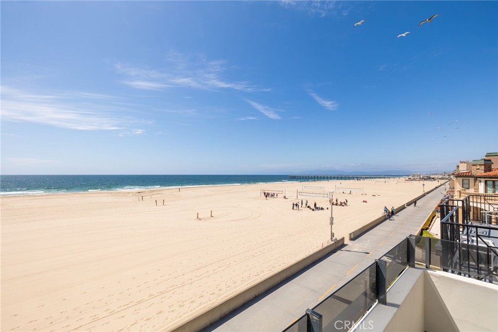 Beach and ocean view from a balcony, with volleyball courts and a beachfront walkway.