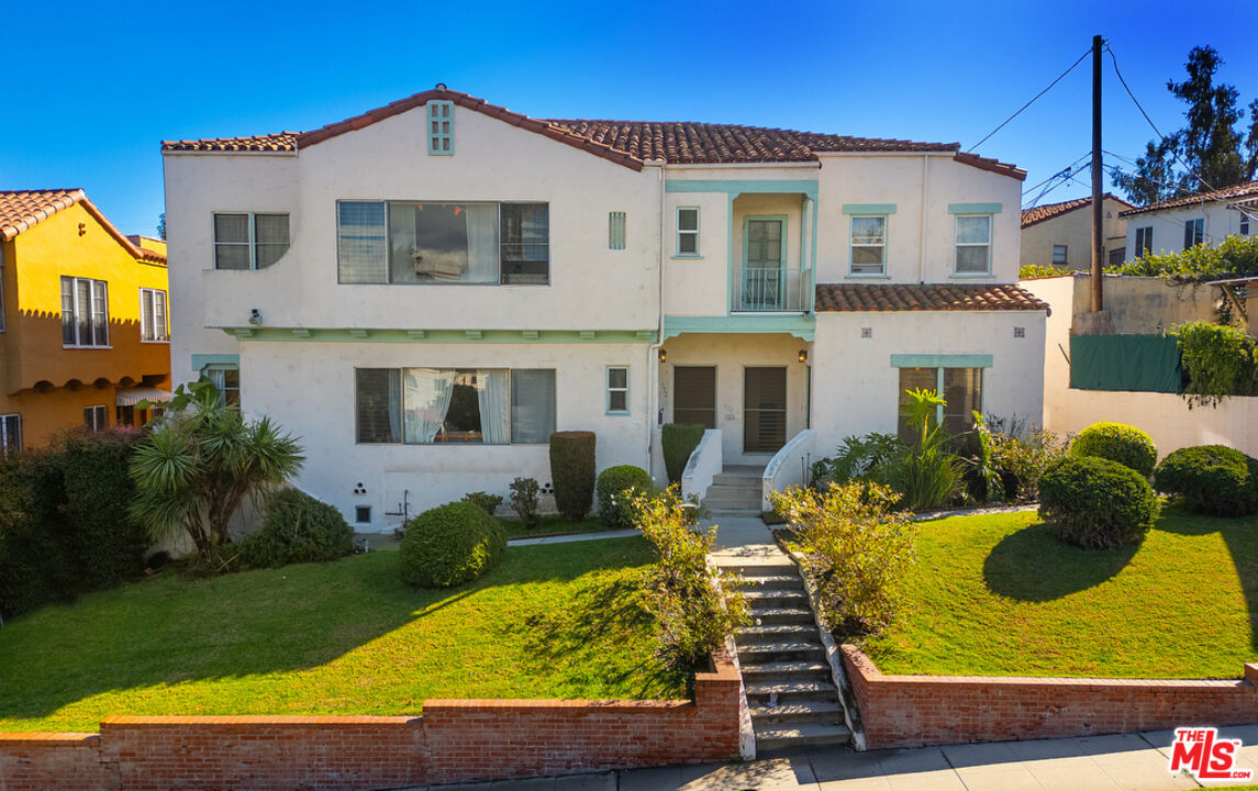 White two-story home with a turquoise entry balcony, tiled roof, and front lawn.