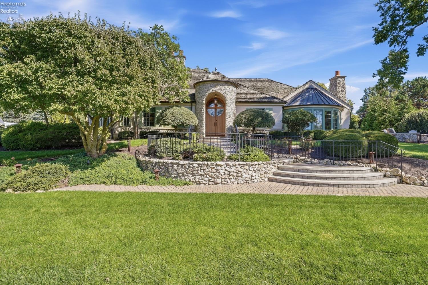 Home with a stone entry tower, rounded bay windows, and curved front steps amid landscaped grounds.