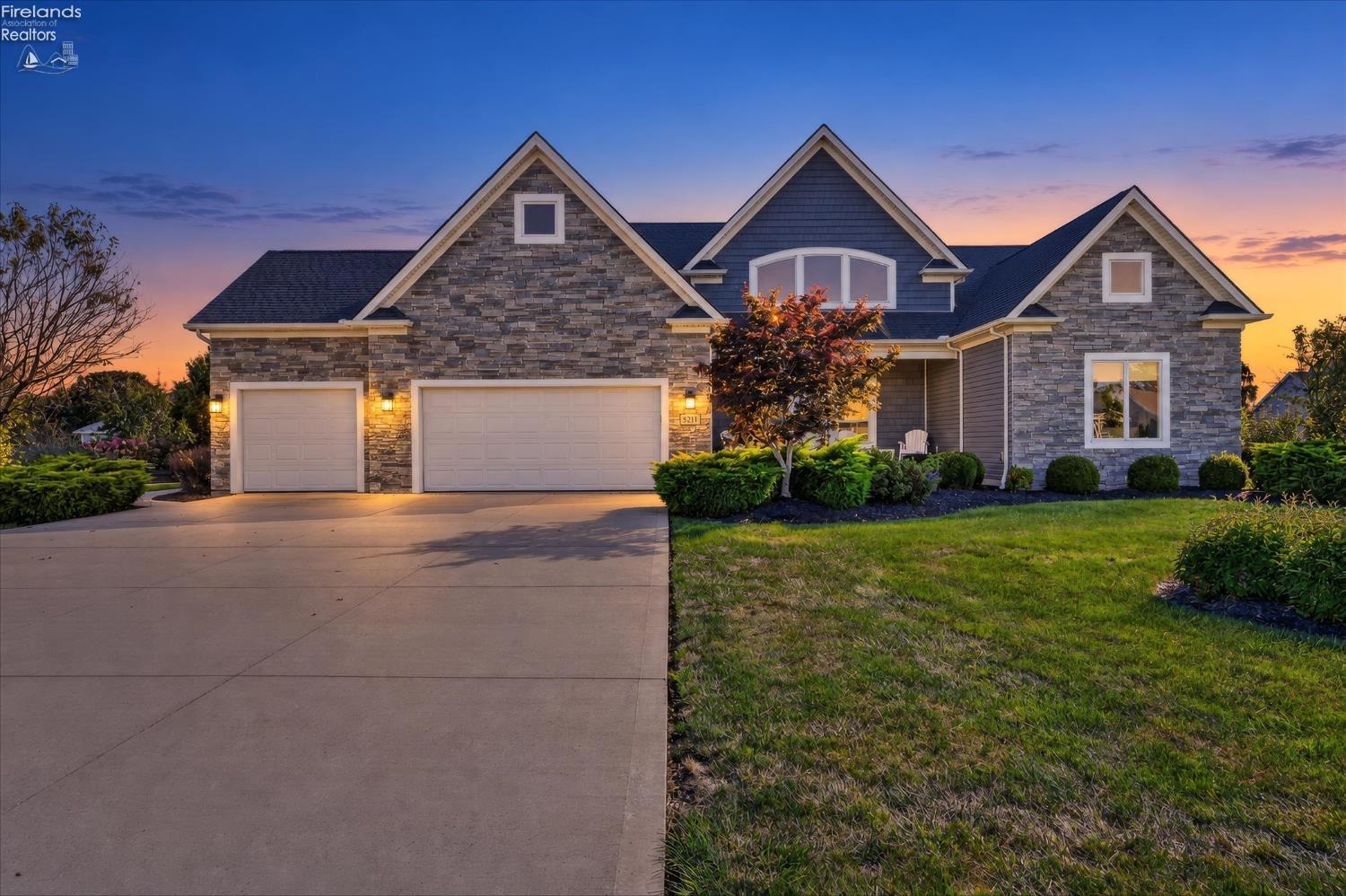 Two-story stone-and-blue-sided home with attached garages and landscaped front yard at dusk.