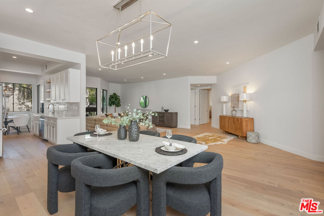 Dining area with a marble table and gray chairs opening to a bright kitchen and living room.