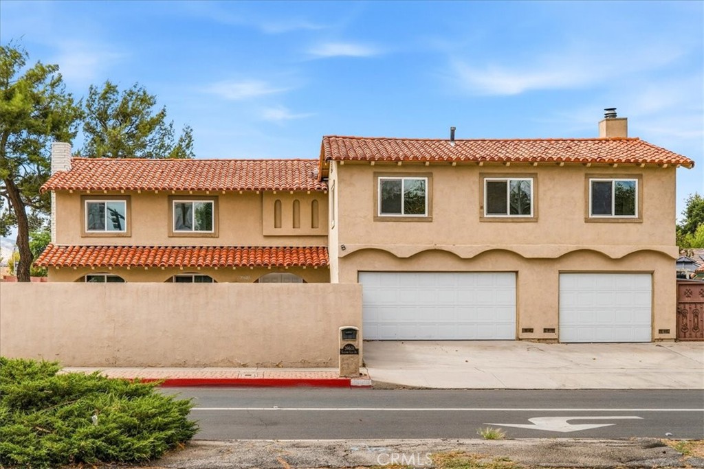 Two-story stucco home with a red tile roof, front wall, and two garage doors.