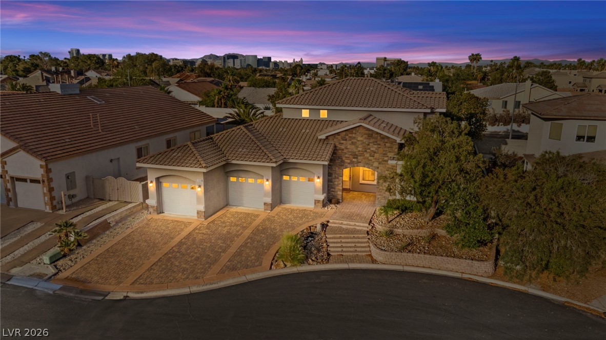 Spring Valley home with stone accents, three garages, and an illuminated entry at dusk.