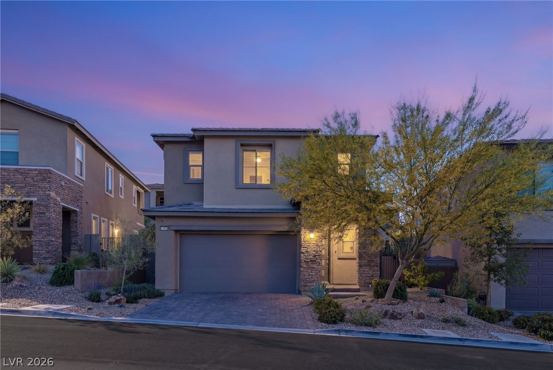 Two-story stucco home with stone accents, an attached garage, and desert landscaping at dusk.