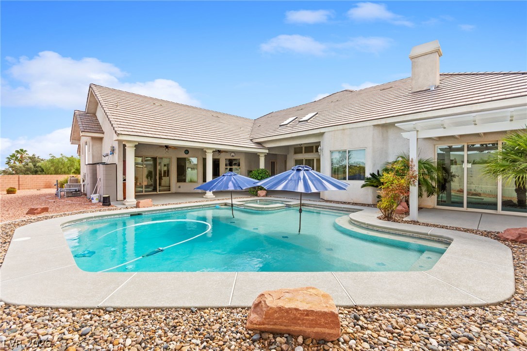 Backyard pool with blue shade umbrellas beside a single-story stucco home and desert landscaping.