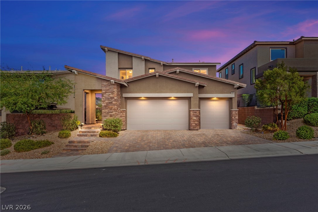 Modern two-story home with stone accents, a double garage, and desert landscaping at dusk.