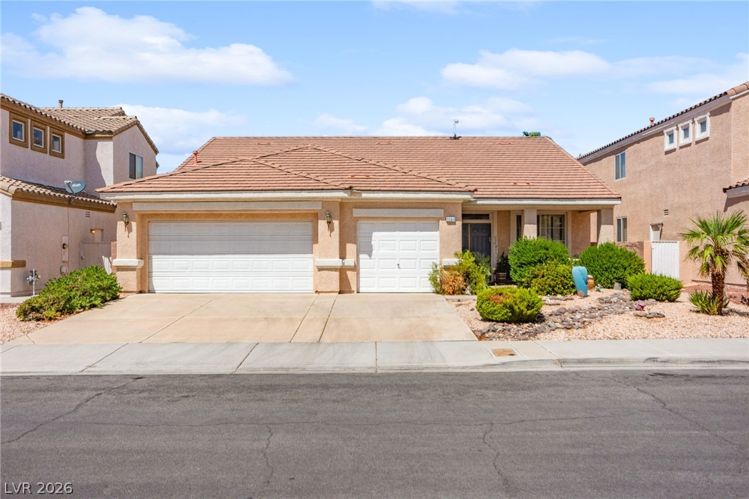 Single-story stucco home with a red tile roof, two garage doors, and desert landscaping.