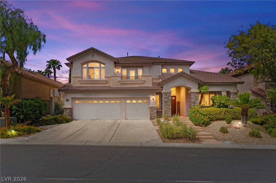 Two-story stucco home with an arched entry, two-car garage, and desert landscaping at dusk.