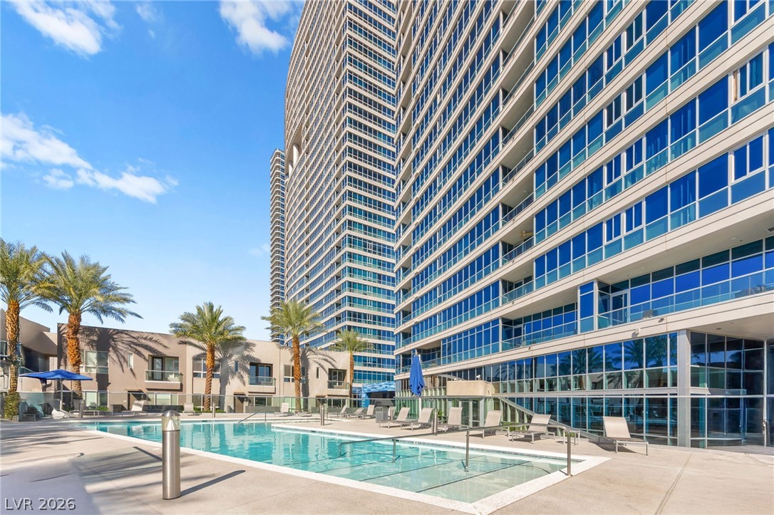 Panorama Towers pool beside glass high-rises, with palm trees and lounge chairs.