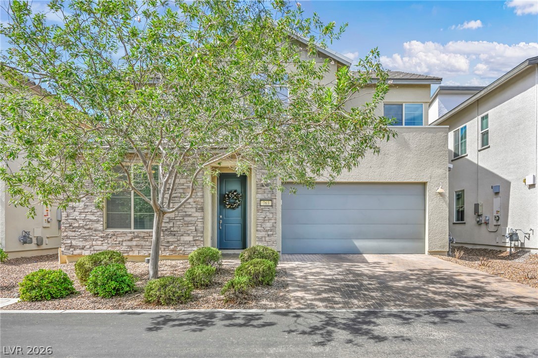 Two-story stucco home with stone accents, a teal front door, and desert landscaping.