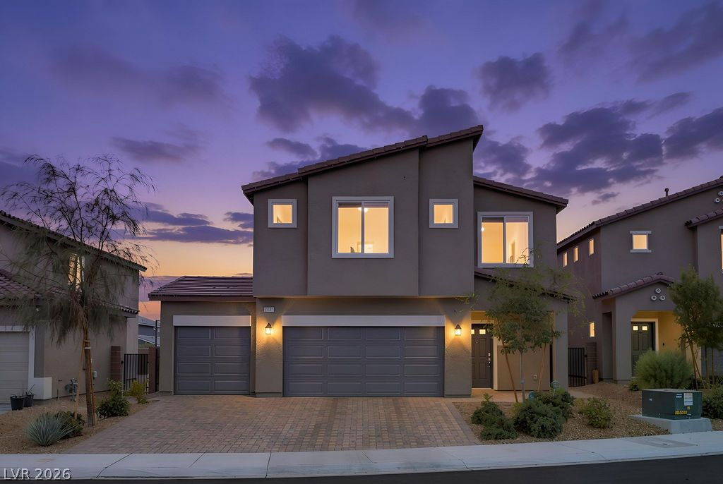 Two-story Azure Park home with attached garages and illuminated windows at dusk.
