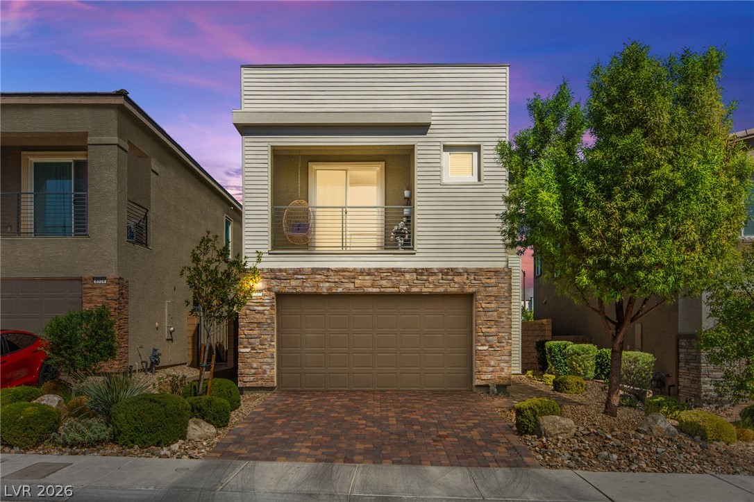 Modern two-story home with a stone facade, balcony, two-car garage, and desert landscaping at dusk.