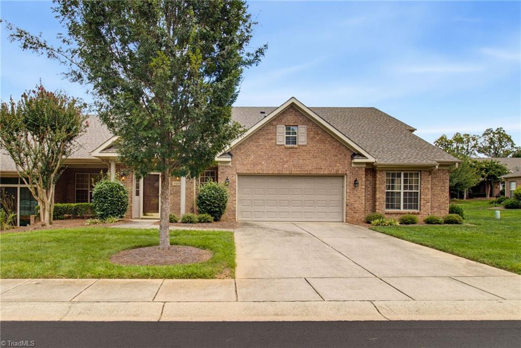 Brick home with attached two-car garage, gabled roof, and mature tree in the front yard.