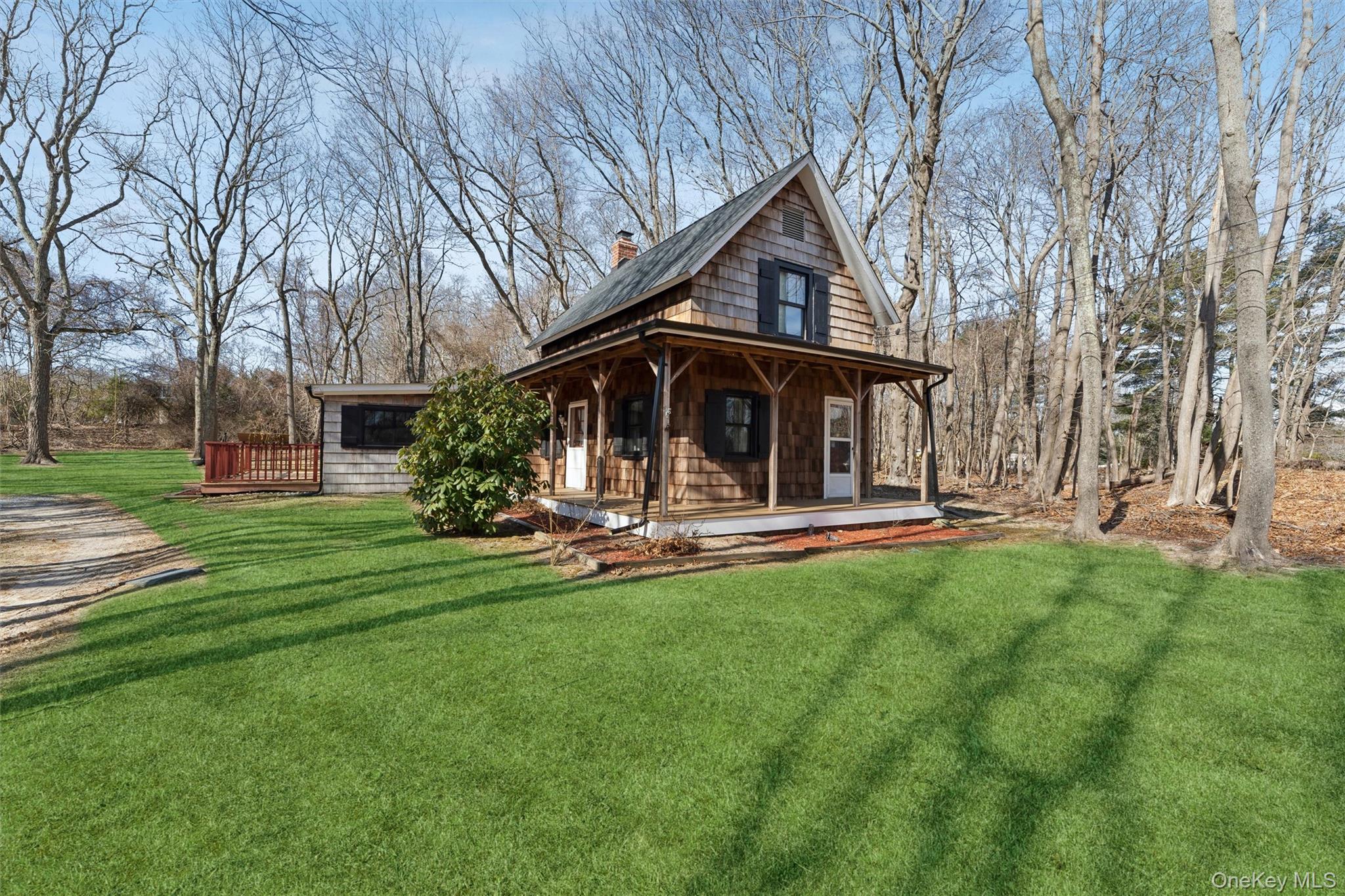 Cedar-shingle home with a steep gabled roof and covered porch on a lawn among leafless trees.