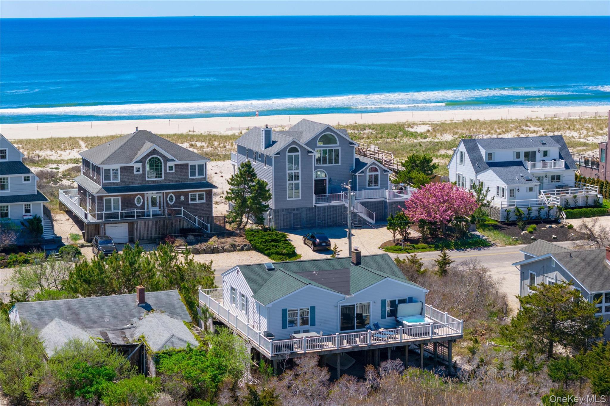 Coastal homes beside a sandy beach and ocean, viewed from above.